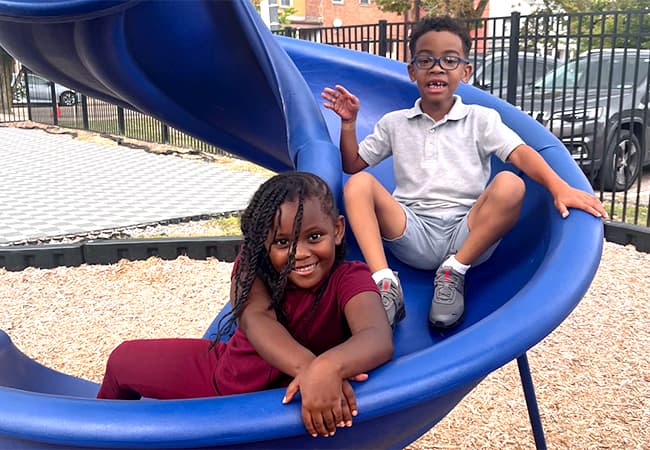 A boy and girl sitting together at the bottom of a slide.