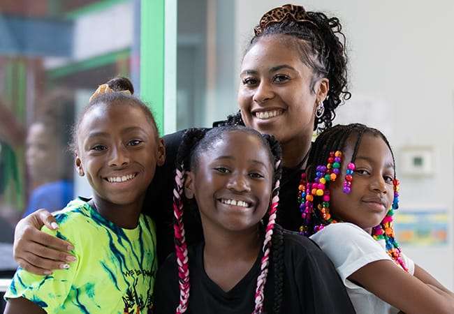 A smiling teacher poses with three female students.