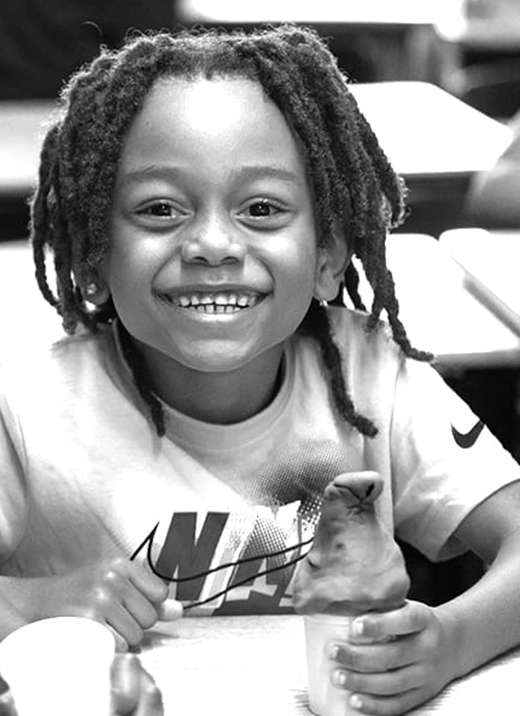 A young boy sitting a table smiles for the camera.